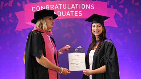 Two people in graduation attire; one hands a certificate to the other